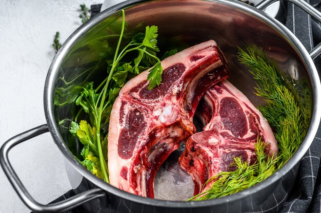 Carne di agnello fresca cruda sulle ossa con le spezie e condimento in una casseruola. Sfondo grigio. Vista dall'alto