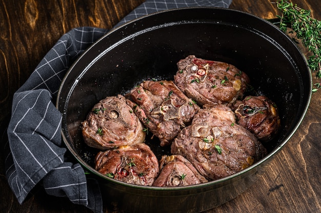 Carne di collo di agnello stufata in padella con erbe aromatiche. fondo in legno. Vista dall'alto.