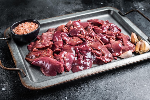 Carne di fegato di pollo cruda in vassoio d'acciaio con spezie Sfondo nero Vista dall'alto