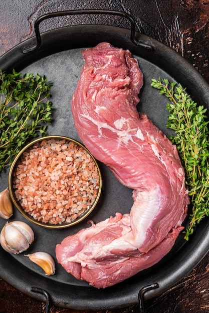 Carne di filetto di filetto di maiale crudo crudo su un vassoio da cucina con aglio timo e sale marino Sfondo scuro Vista dall'alto