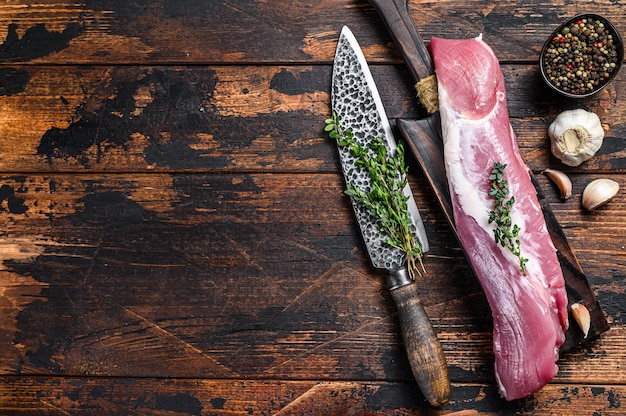 Carne di filetto di maiale crudo fresco su un tagliere con mannaia. Fondo in legno scuro. Vista dall'alto. Copia spazio.