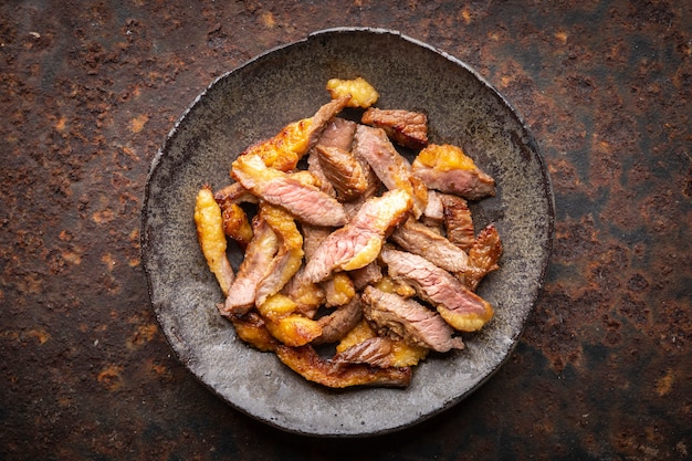 Carne di filetto di manzo alla griglia affettata succosa in piatto stile wabi sabi su sfondo arrugginito, vista dall'alto