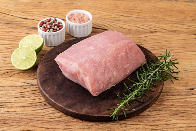 Carne di lonza di maiale cruda su tavola di legno con condimenti.
