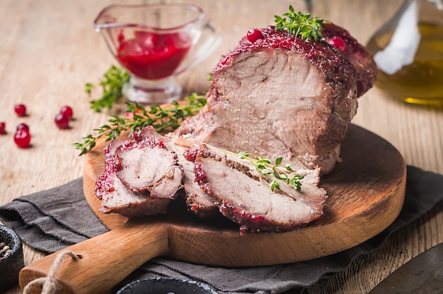 Carne di maiale al forno con salsa di mirtilli e timo su concetti di superficie in legno di cibo per le vacanze