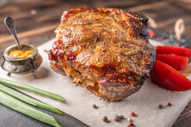 Carne di maiale al forno fatta in casa con verdure e spezie su un tagliere su un fondo di legno.