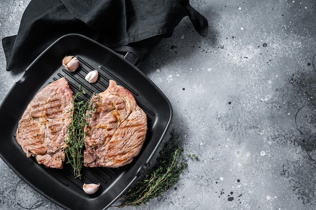 Carne di maiale alla griglia Bistecche di carne di filetto su padella per griglia Sfondo grigio Vista dall'alto Spazio di copia