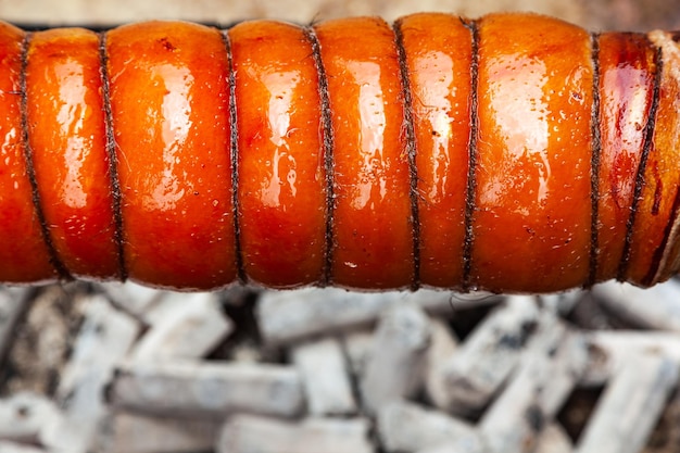 Carne di maiale con pancetta e pelle legata con corde alla griglia sul primo piano dei carboni