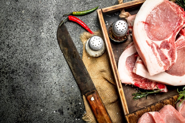 Carne di maiale cruda con erbe e spezie in un vassoio sul tavolo rustico.