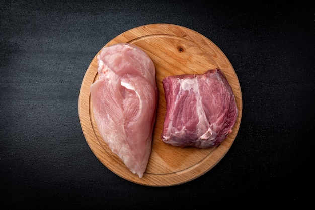 Carne di maiale cruda e filetto di pollo sulla tavola nera.