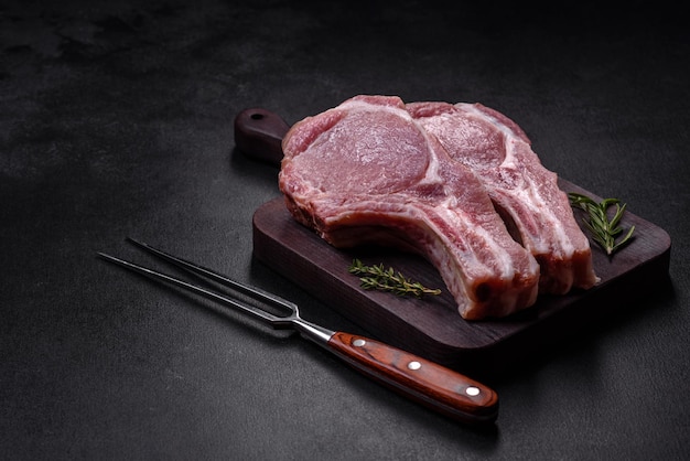 Carne di maiale cruda fresca sulle costole con spezie ed erbe aromatiche su un tagliere di legno su uno sfondo di cemento scuro