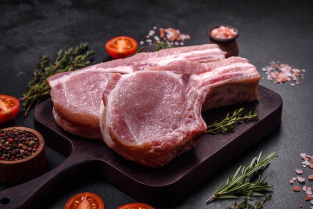 Carne di maiale cruda fresca sulle costole con spezie ed erbe aromatiche su un tagliere di legno su uno sfondo di cemento scuro