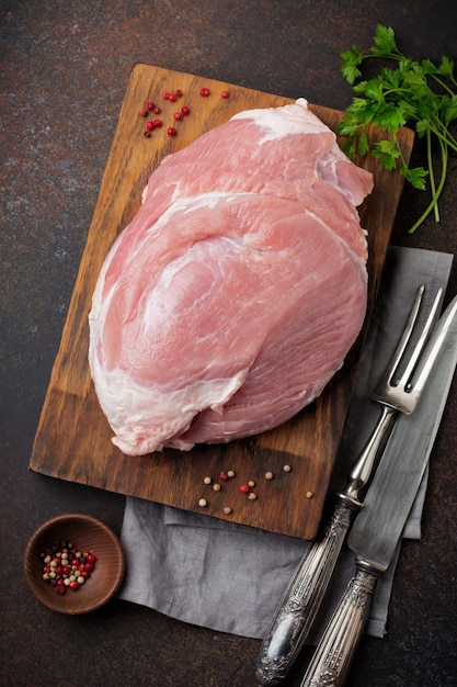 Carne di maiale cruda su un tagliere di legno su ardesia, pietra o cemento.