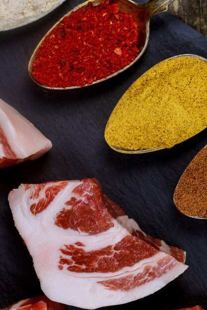 Carne di maiale cruda su un tavolo nero e con diverse spezie