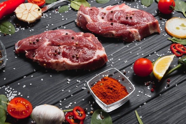 Carne di maiale cruda sul tagliere di legno al tavolo della cucina per cucinare bistecca di maiale arrosto o alla griglia con ingredienti erbe e spezie, carne di maiale fresca