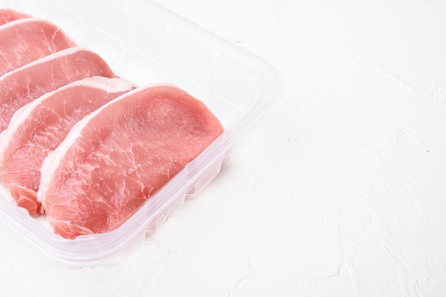 Carne di maiale. Set di bistecche di maiale fresche, in un contenitore di plastica, su sfondo di tavolo in pietra bianca, con spazio di copia per il testo