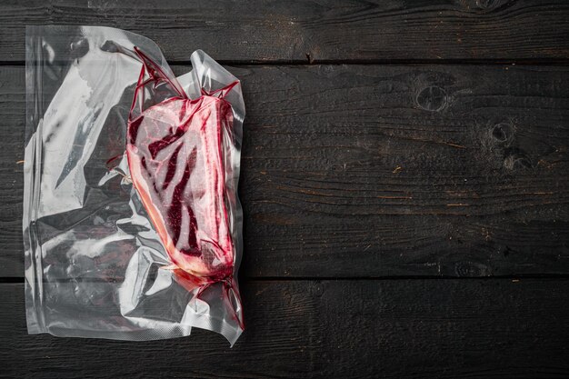 Carne di manzo cruda Club o controfiletto sulla bistecca di osso in confezione ermetica di plastica su sfondo tavolo in legno nero vista dall'alto piatto disteso con spazio di copia per il testo