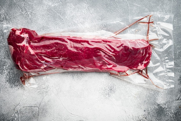 Carne di manzo fresca e cruda. Intero pezzo di filetto in set di sacchetti di plastica sottovuoto, su tavolo in pietra grigia, vista dall'alto piatta