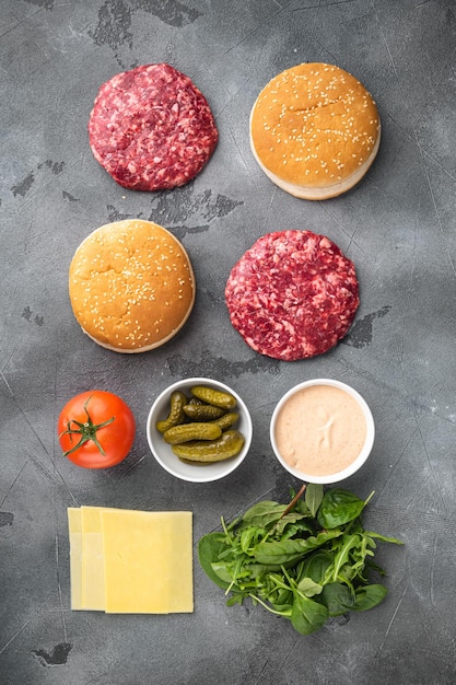 Carne di manzo macinata cruda Cotolette di bistecca di hamburger con ingredienti e panini su sfondo di pietra grigia vista dall'alto piatto