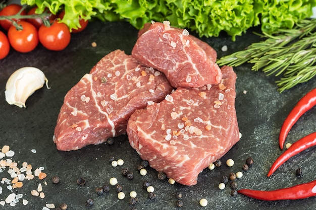 Carne di manzo marmorizzata fresca cruda, condimenti su tagliere di pietra scura