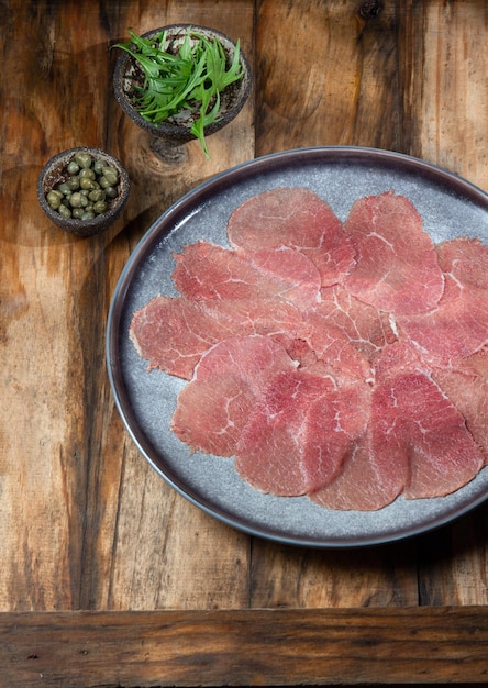 Carne di manzo marmorizzata per carpaccio con ingredienti rucola e capperi su piastra grigia in legno vista dall'alto