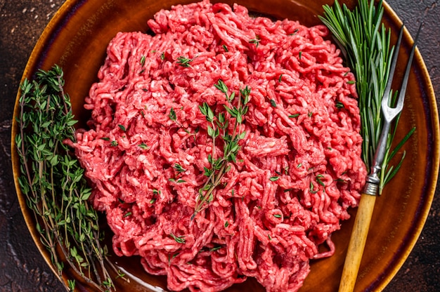 Carne di manzo o vitello macinata cruda su un piatto rustico con erbe