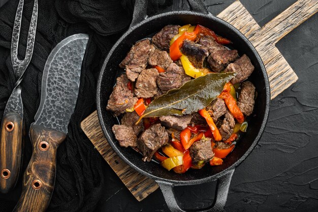 Carne di manzo stufata con patate, carote e spezie adagiate in una padella di ghisa su sfondo di pietra nera vista dall'alto piatto