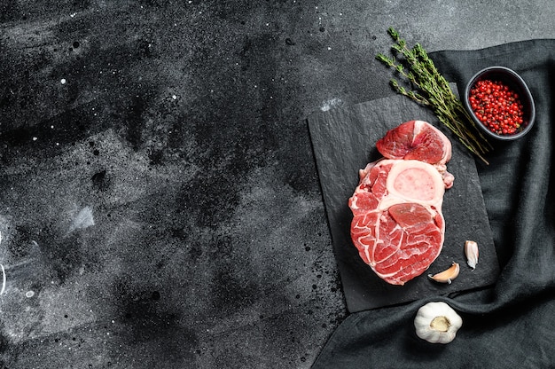 Carne di Osso Buco. Stinco di vitello crudo tagliato a croce e condimenti per la cottura di Osso Buco. Sfondo nero