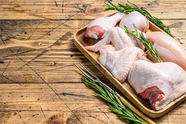 Carne di pollo crudo fresco, ali, petto, coscia e cosce su un vassoio di legno.