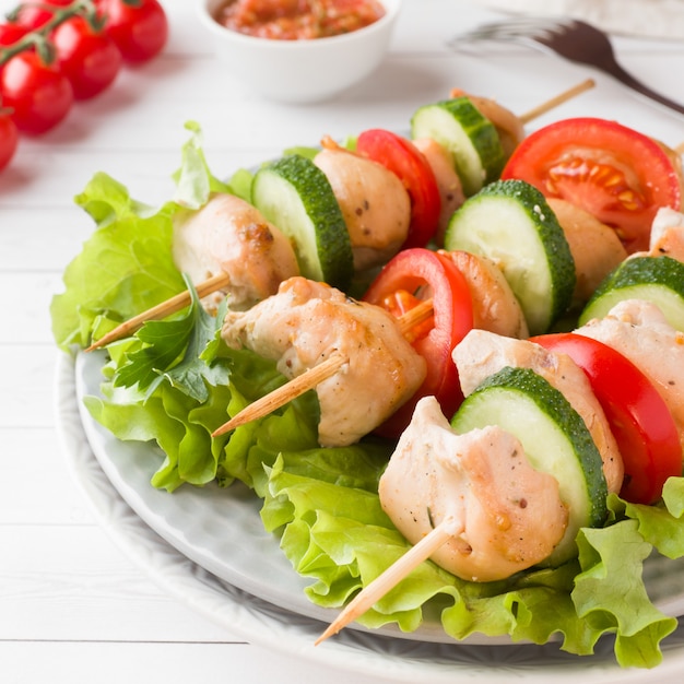 Carne di pollo kebab tradizionale con pomodori, cetrioli e erbe fresche su un piatto.