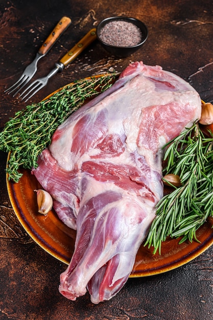 Carne di spalla di agnello crudo fresco intero su un piatto. Fondo in legno scuro. Vista dall'alto.