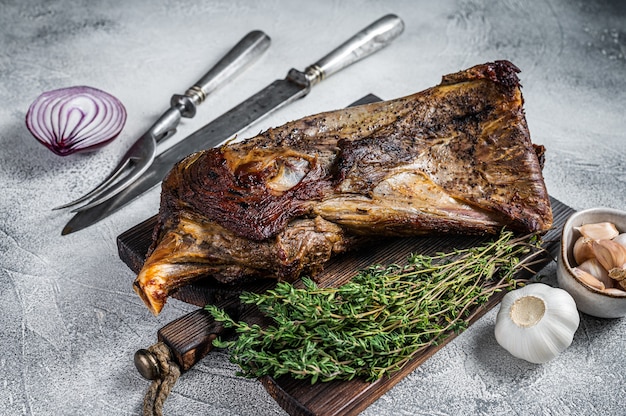 Carne di spalla di agnello o capra alla griglia su una tavola di legno con coltello e forchetta per carne. Sfondo bianco. Vista dall'alto.