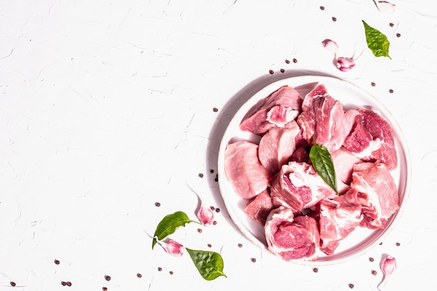 Carne di suino cruda a dadini con sommacco secco, aglio fresco e foglie di basilico. Concetto di cucina sana, luce dura alla moda, ombra scura. Sfondo bianco stucco, vista dall'alto