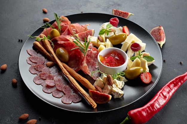 Carne e formaggio assortiti, su un piatto nero con erbe e frutti di bosco