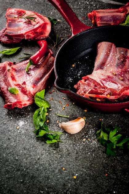 Carne fresca cruda, agnello crudo o costolette di manzo con peperoncino, aglio e spezie con padella padella su pietra scura,