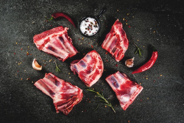 Carne fresca cruda, agnello crudo o costolette di manzo con peperoncino, aglio e spezie su fondo di pietra scura