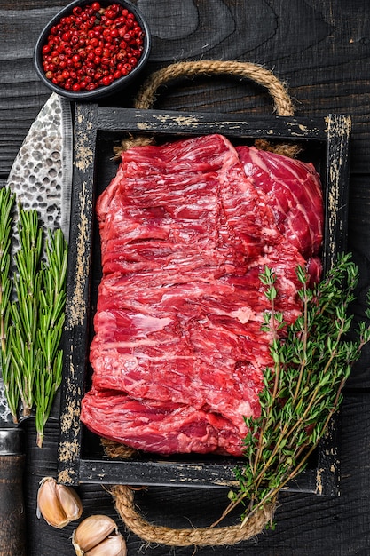 Carne fresca cruda del taglio del petto di manzo con le erbe in un vassoio di legno. Fondo in legno nero. Vista dall'alto.