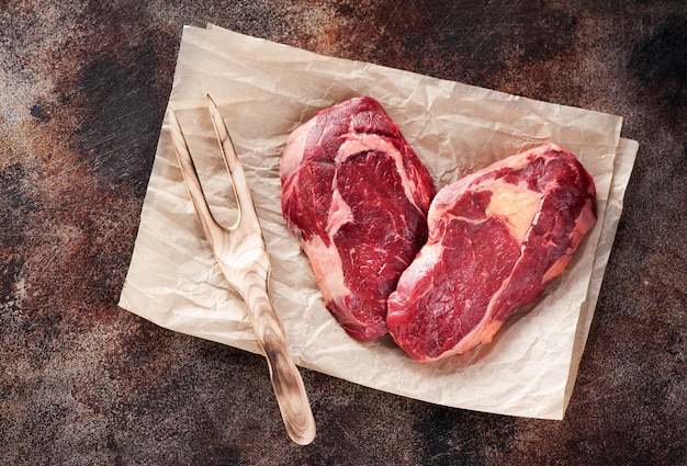 Carne fresca cruda Ribeye Steak a forma di cuore su carta marrone su sfondo marrone cemento vista dall'alto