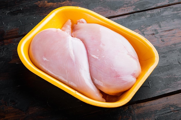 Carne fresca del petto di pollo in vassoio aperto, su fondo di legno scuro