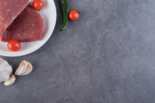 Carne fresca e cruda con pomodorini rossi posti sul tavolo in pietra.