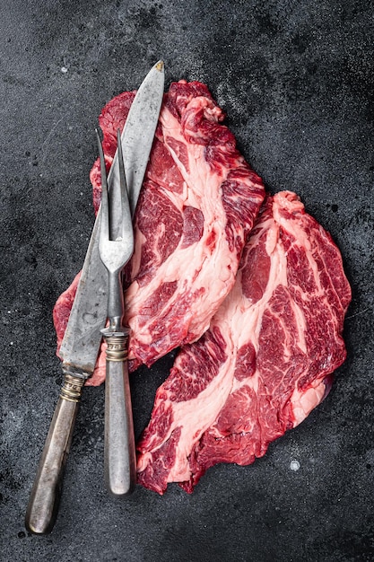 Carne fresca marmorizzata Bistecche con coltello da carne e forchetta bistecca di manzo da tavola Sfondo nero Vista dall'alto