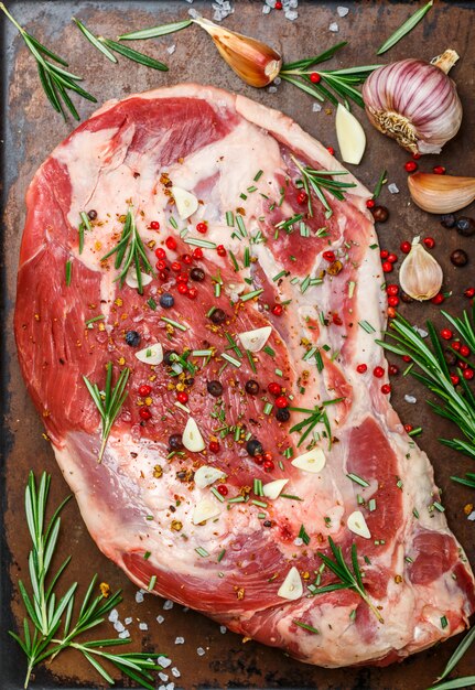 Carne fresca. Spalla di agnello cruda pronta per la cottura con aglio, rosmarino, ginepro, pepe e sale