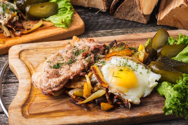 Carne fritta con patate fritte, uova e cetrioli salati su tavola di legno.
