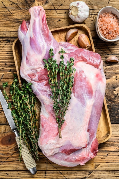 Carne intera di coscia di capra cruda su un vassoio di legno