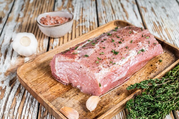 Carne intera di lonza di maiale disossata cruda con timo e sale su tavola rustica.