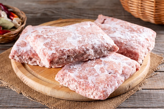 Carne macinata congelata, carne di maiale macinata su una tavola di legno. Pollo macinato inclusi dorsi, colli, fegato e cuore. Cibo surgelato. Concetto di dieta crudista per gatti, cani e animali domestici. Dispensa