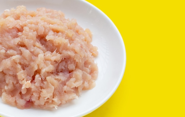 Carne macinata di filetto di pollo in piastra bianca su sfondo giallo.