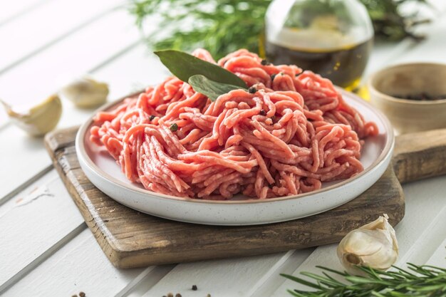 Carne macinata di manzo cruda fresca con erbe aromatiche e rosmarino su tavola di legno su sfondo chiaro menu banner ricetta posto per testo vista dall'alto