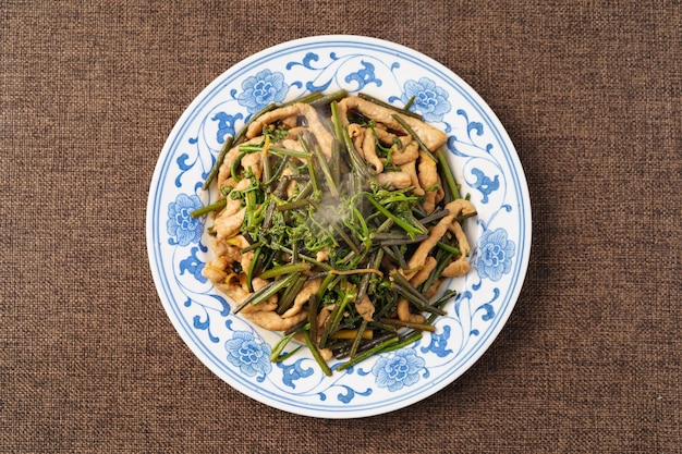 Carne saltata in padella con felce di montagna su sfondo monocromatico