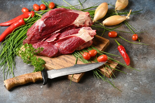 Carne scura fresca con ingredienti per cucinare sul tagliere di legno marrone.