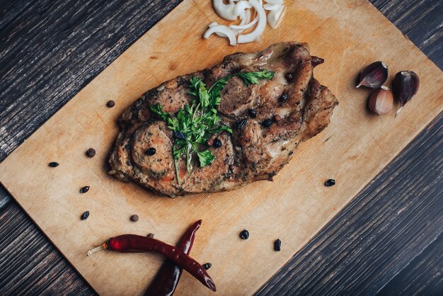 Carne suina cotta su un tagliere di legno su un tavolo con pepe, aglio, cipolla